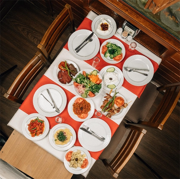 İzmir'in en iyi restoranlarından biri olan Gandi'nin Yeri'nde, kırmızı beyaz çizgili masa örtüsüyle bezeli ahşap masada çöp şiş, ızgara köfte, sucuk, salata, haydari ve çeşitli zeytinyağlı mezelerle dolu tabaklar, geleneksel bir meyhane ziyafetini göz alıcı bir şekilde sunuyor.