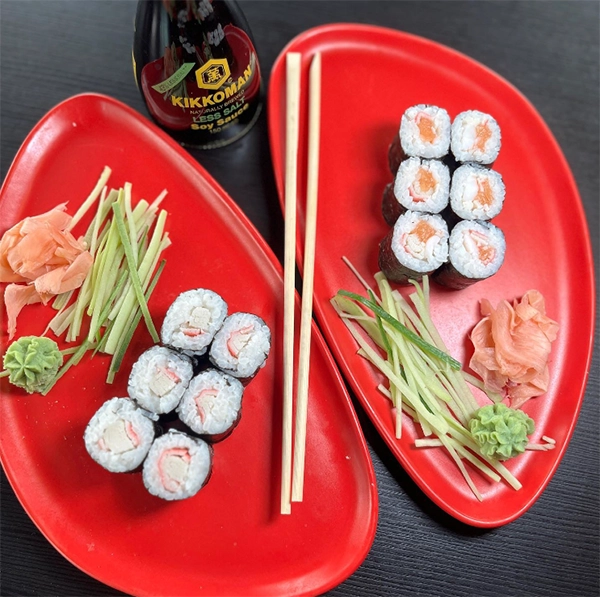 Kırmızı renkli iki tabakta, somon ve yengeç surimili makilerin yanı sıra zencefil, wasabi, ince salatalık dilimleri ve soya sosuyla birlikte sunulan bu iştah açıcı sushi düzenlemesi, İzmir'in en iyi sushi restoranları rehberindeki zengin Uzak Doğu lezzetlerini vurguluyor.