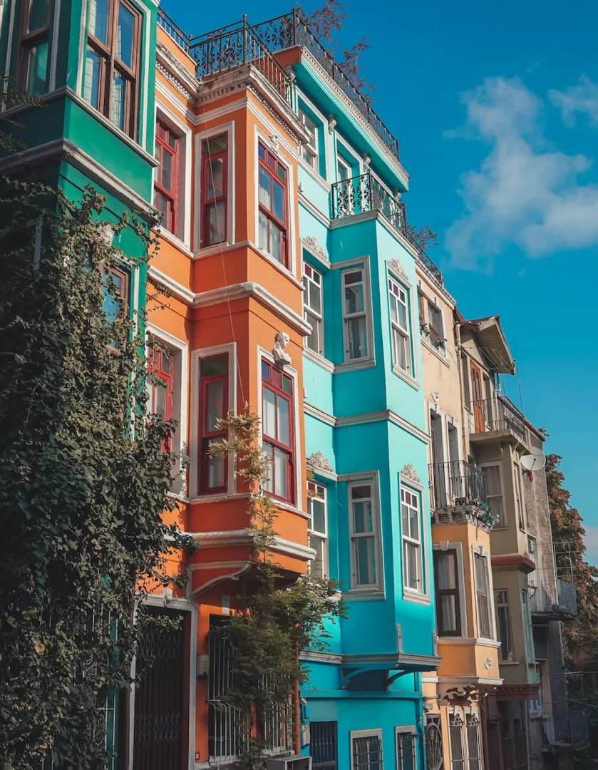 İstanbul Balat'ta yer alan, turuncu, turkuaz ve yeşilin canlı tonlarında boyanmış, tarihi cumbalı pencerelere ve detaylı süslemelere sahip sıra sıra evler, masmavi bir gökyüzünün altında büyüleyici bir manzara oluşturuyor.
