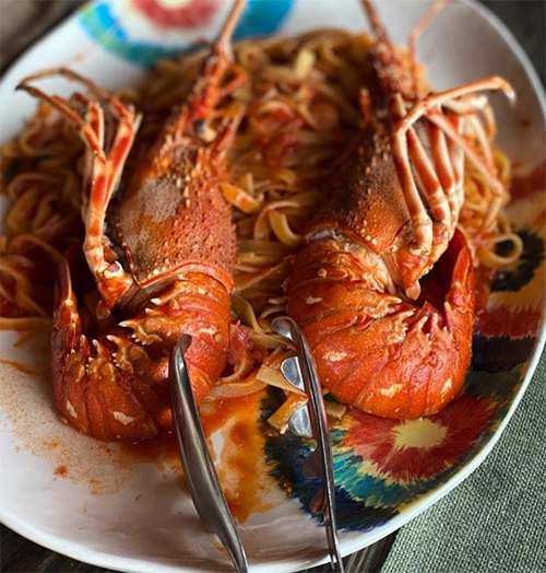 Domates soslu makarnanın üzerinde servis maşasıyla birlikte sunulan, parlak turuncu renkli iki bütün istakozun yer aldığı renkli desenli bir tabak, İzmir'in en iyi restoranları arasında deniz ürünleri ağırlıklı bir seçeneği vurguluyor.