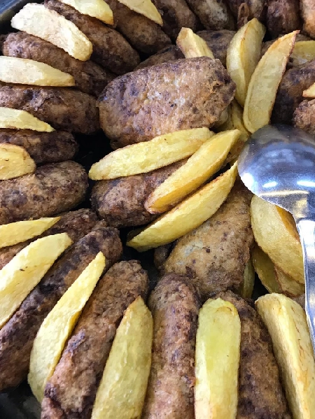 İzmir'in en iyi esnaf lokantalarından Özüm Lokantası'nda servis edilen, bol porsiyonlu kahverengi kızarmış köftelerin, altın rengi elma dilim patateslerle ve metal bir servis kaşığıyla dolu bir kapta yakın çekim görüntüsü.