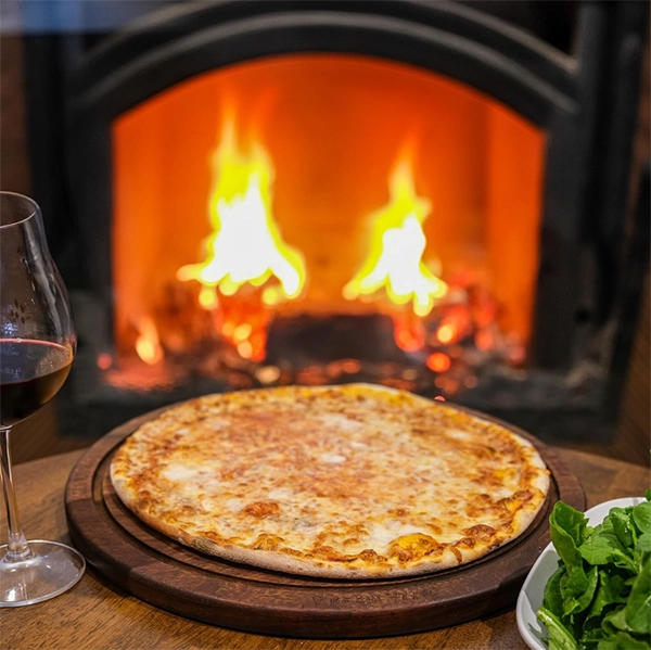 İzmir'in popüler restoranlarından birinde, odun ateşinin huzurlu parıltısıyla ısınan bir masada, üzerinde bolca erimiş peynir bulunan, iştah açıcı yuvarlak bir pizza, yanında şık bir kadeh dolusu kırmızı şarap ve yeşil roka salatası servis edilmiş keyifli bir an.