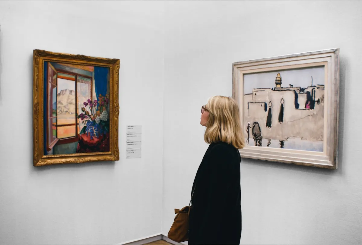 Sarışın, gözlüklü bir kadın, sonbahar sergi rotalarından birinde olduğunu gösterircesine, bir sanat galerisinde duvarındaki minareli bir tabloya dikkatle bakarken, solunda çiçekli bir pencere resmi de görülüyor.