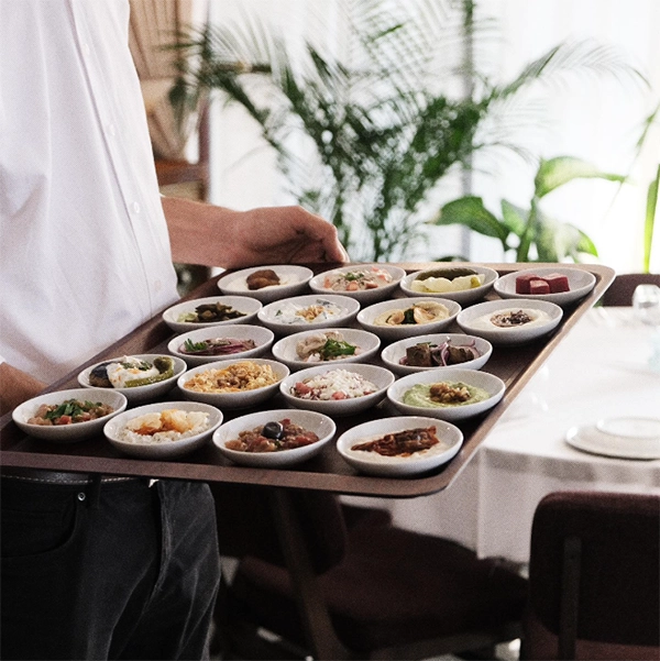 İzmir'in en iyi restoranları listesinde yer alan Yasef'in Meyhanesi'nde, beyaz gömlekli bir garson, masaya servis edilmek üzere, çeşit çeşit iştah açıcı soğuk mezenin özenle dizildiği koyu renk, büyük bir tepsi taşıyor.