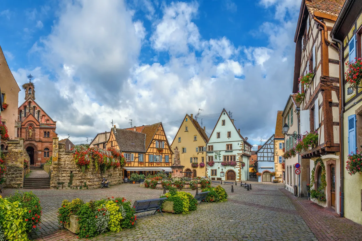 Alsace bölgesinde Eguisheim köyünde renkli yarı ahşap evler ve çiçekli meydan
