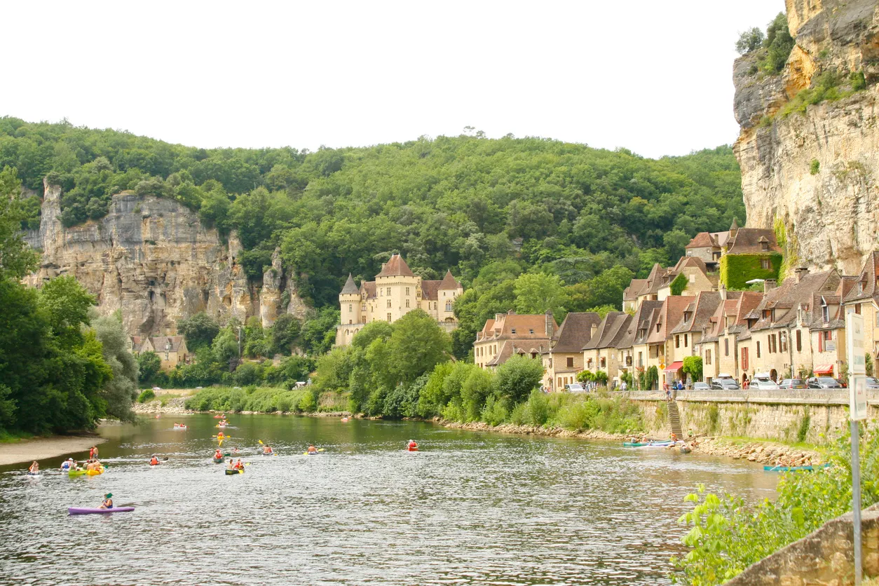 Dordogne bölgesinde La Roque-Gageac kasabasında nehir boyunca uzanan taş evler ve kano yapanlar
