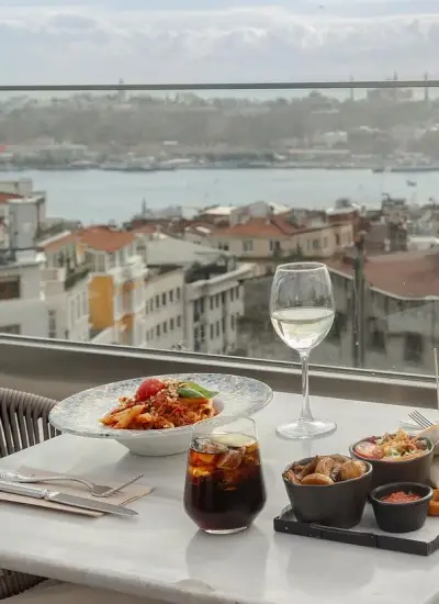 Boğaz manzaralı terasta şık bir sofrada makarna, meze tabakları ve beyaz şarap eşliğinde fine dining deneyimi: Barnathan İstanbul manzaralı restoran.
