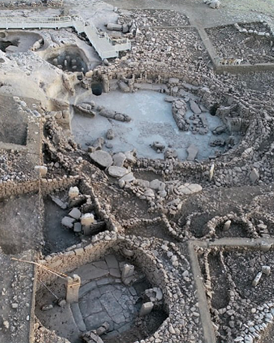 Karahantepe'deki geniş arkeolojik kazı alanının kuşbakışı görüntüsü, toprak ve taş kalıntılarla dolu arazide dairesel planlı, karmaşık taş duvar yapılarını ve henüz tamamen açığa çıkmamış tarihi gizemleri gözler önüne seriyor.