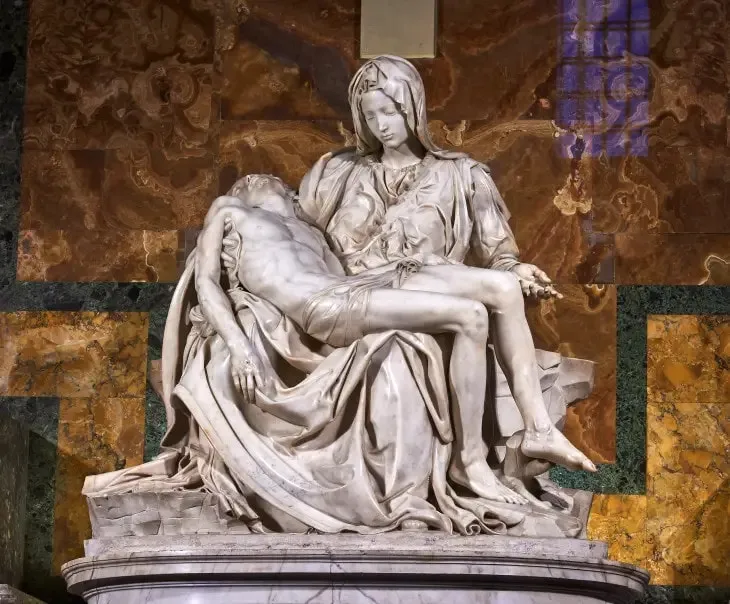 Michelangelo'nun başyapıt eserlerinden biri olan, Meryem Ana'nın kucağında ölü İsa'yı tuttuğu beyaz mermer Pietà heykeli, kıvrımlı detayları ve derin duygusal ifadesiyle öne çıkarken, arka planda kahverengi ve yeşil tonlarda damarlı mermer duvarlar görülüyor.