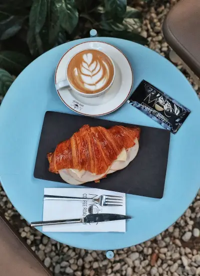 MOC Coffee Roasters'ta mavi masa üzerinde servis edilen kruvasan ve latte; rahat bir kahve molası sunan atmosfer.