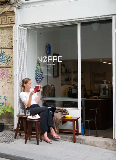 stanbul sokaklarında butik kahve mekânı Nørre önünde kahvesini yudumlayan kadın, sade ve modern dış cephe tasarımıyla dikkat çeken kafe atmosferi.