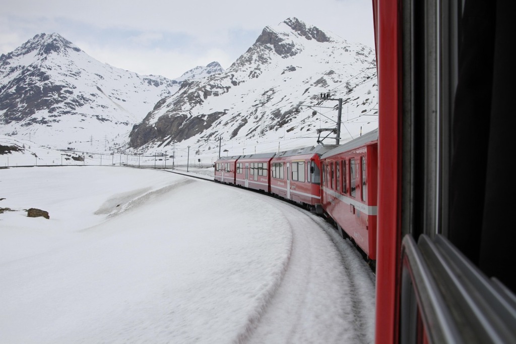 İsviçre’nin Engadin vadisindeki Piz Bernina manzarasında ilerleyen kırmızı Bernina Ekspresi – karlı Alp dağları arasında unutulmaz bir tren yolculuğu