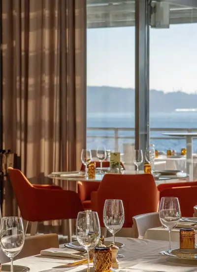 Boğaz manzaralı cam cepheli şık restoran Modern'de gün batımı ışığıyla aydınlanan sofistike masa düzeni.