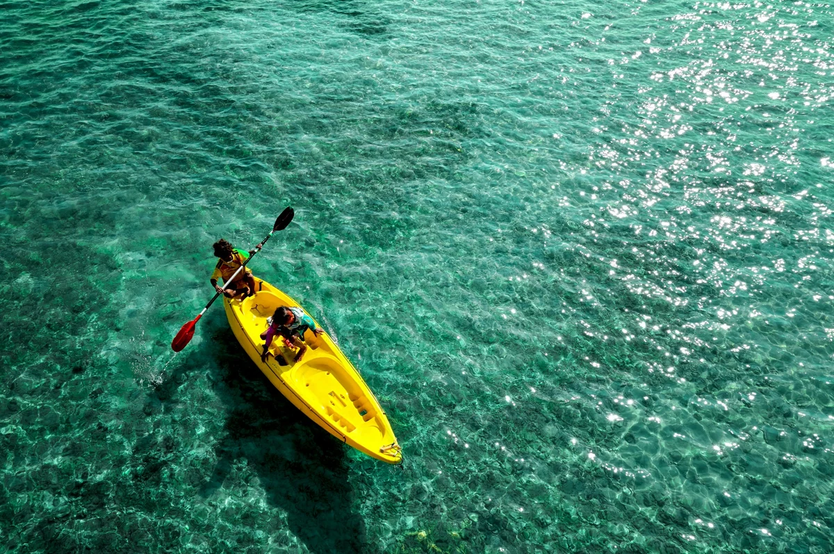 Güneşin pırıl pırıl parladığı berrak turkuaz sular üzerinde, iki kişinin sarı bir deniz kayağında keyifle kürek çekerek ilerlediği, Türkiye'de deniz kayağı deneyimlerinin güzelliğini anlatan kuşbakışı bir görüntü.