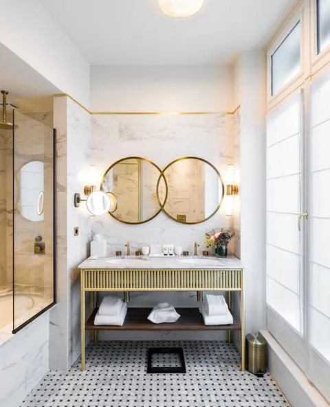 Paris'in beş yıldızlı butik oteli Hotel Grand Powers'ın Art Deco detayları ve mermer yüzeyleriyle dikkat çeken lüks banyosunda, altın çerçeveli iki yuvarlak ayna, çift lavabo ve şık armatürler modern ve konforlu bir konaklama deneyimi sunuyor.