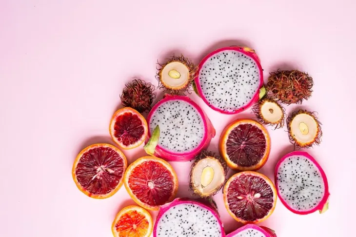 Ejder meyvesi, kan portakalı ve rambutan gibi tropikal ve antioksidan zengini meyveler pembe arka planda.