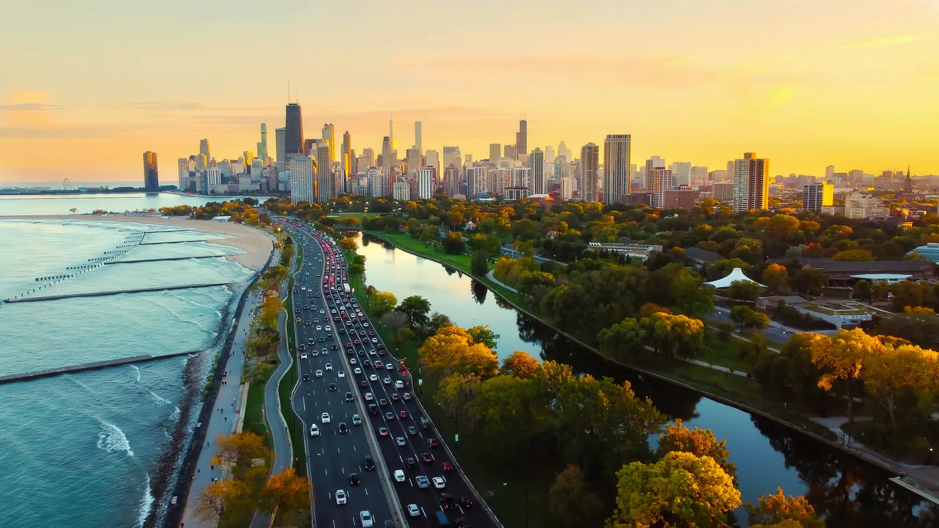 Güneşin altın rengi ışıkları altında, Michigan Gölü kıyısı boyunca uzanan yoğun trafikli otobanın, yemyeşil ağaçların ve sakin bir nehrin eşlik ettiği Chicago silüeti, Amerika bahar rotası için göz alıcı bir şehir manzarası sunuyor.