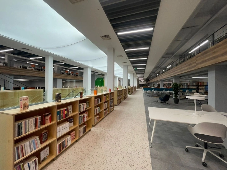 Geniş ve aydınlık İBB Habitat Kütüphanesi'nin içinden çekilen bu fotoğrafta, modern tasarımıyla öne çıkan uzun kitap rafları, çeşitli çalışma masaları ve rahat koltuklarla donatılmış okuma alanları, yukarı katlara çıkan bir yürüyen merdiven ve gençlik platformuna işaret eden dinamik bir yeşil dekoratif öge, İstanbul'un en iyi kütüphaneleri arasında yer alan bu yeni nesil bilgi merkezinin ilham verici ve ferah atmosferini sergiliyor.