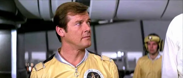 James Bond serisinin Roger Moore dönemi filmlerinden Moonraker'da, sarı renkli Drax Enterprise Corporation üniformasıyla yukarı doğru dikkatle bakan aktör, casus filmleri efsanesinin uzay temalı macerasını gözler önüne seriyor.