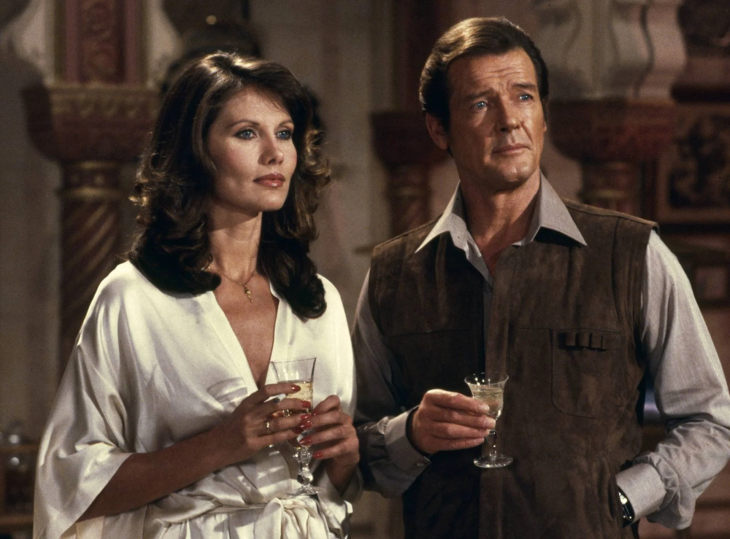 For Your Eyes Only filminden bir sahnede, kahverengi süet yelekli ve açık mavi gömlekli Roger Moore'un canlandırdığı James Bond, beyaz saten bir bornoz giyen Carole Bouquet'in canlandırdığı Melina Havelock ile birlikte, ikisi de şampanya kadehleri tutarak sağa doğru ciddi bir ifadeyle bakıyor.