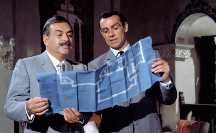 James Bond filmleri serisinin efsanevi ilk Bond'u Sean Connery, eski dönem casusluk filmlerinin ruhuna uygun olarak, yanındaki kişiyle birlikte üzerinde detaylı bir çizim olan mavi bir planı dikkatle inceliyor ve gizemli bir operasyonun veya kilit bir mekânın sırlarını çözmeye çalışırken, izleyiciyi serinin heyecan dolu dünyasına çekiyor.