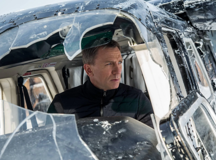 En İyi James Bond Filmleri içeriğimizde Daniel Craig, soğuk ve karlı bir ortamda, hasar görmüş bir helikopterin parçalanmış camlarının arasından ciddi bir ifadeyle dışarıya bakarken serinin yoğun aksiyon dolu sahnelerinden birini yansıtıyor.
