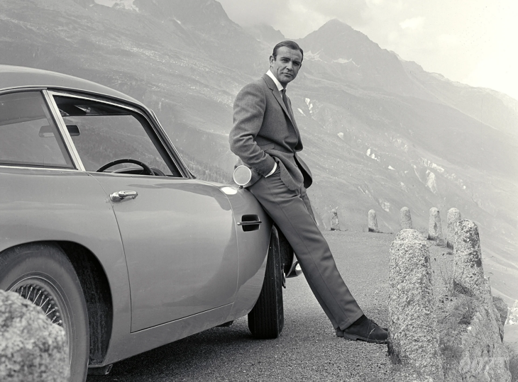 Siyah beyaz fotoğrafta, dağlık bir yol kenarında ikonik Aston Martin marka otomobiline yaslanmış, takım elbiseli, ciddi bakışlı Sean Connery, birçok sinefile göre gelmiş geçmiş en iyi Bond olan karaktere hayat vererek James Bond filmleri evrenine casusluk ruhunu katıyor.