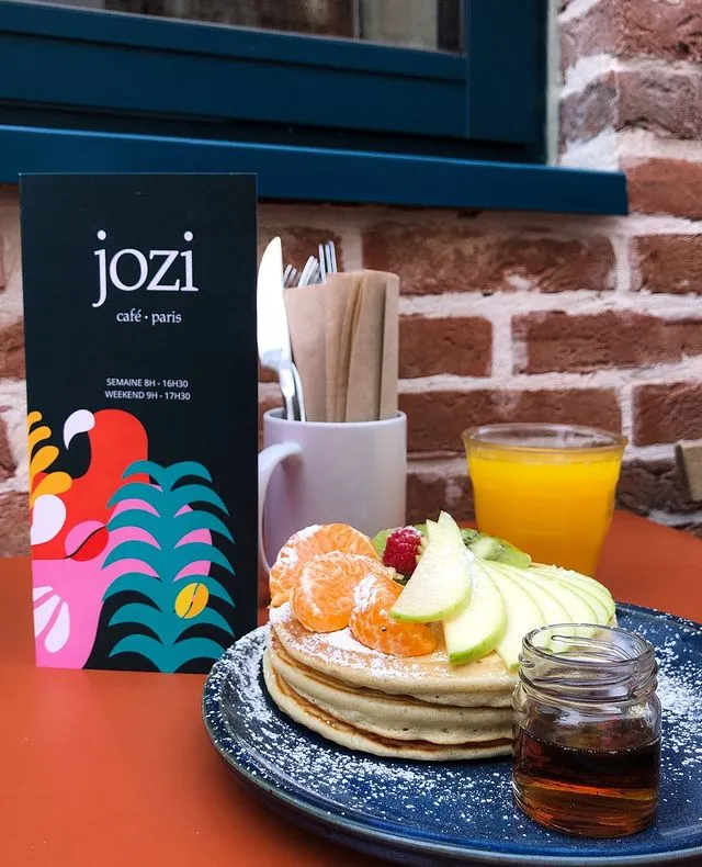 Bir Paris gezi rehberi için ideal bir durak olan Jozi Café'de, taze mandalina, yeşil elma, kivi ve ahududu dilimleriyle zenginleştirilmiş, pudra şekeri serpilmiş iştah açıcı pankekler, yanında akçaağaç şurubu ve portakal suyuyla sunulan keyifli bir brunch sahnesi.