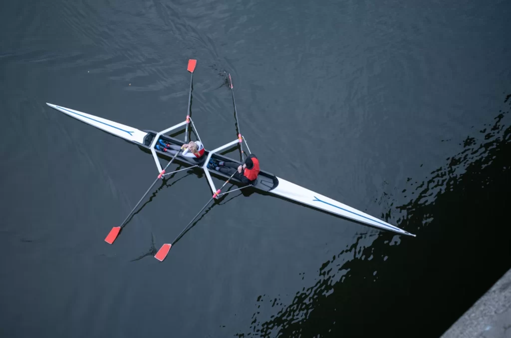 Üstten görünümde, iki sporcunun sculling teknesinde kürek çektiği an; suyun yüzeyinde net izler bırakıyor.