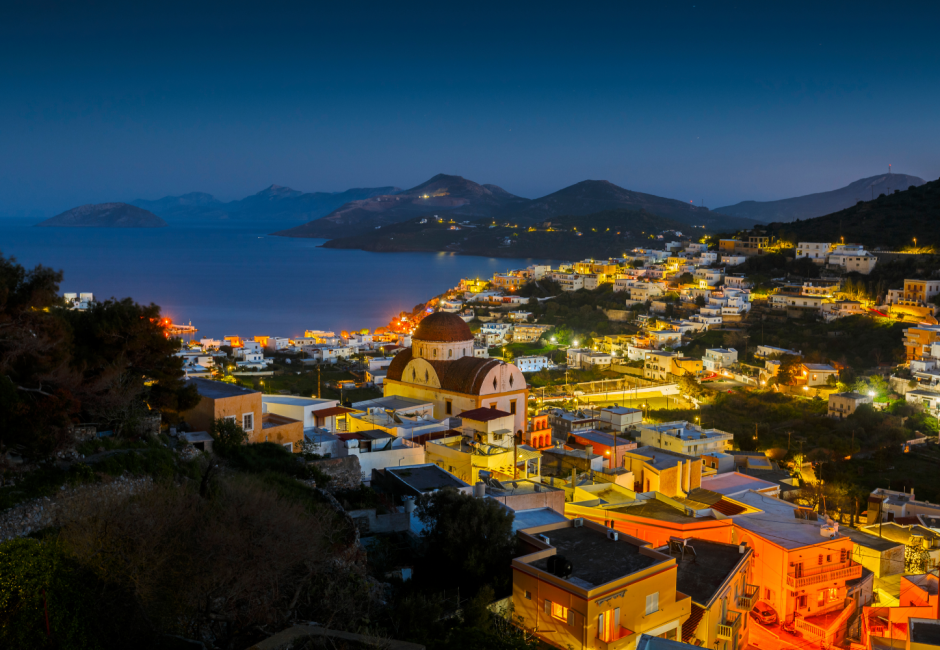 Ege Denizi'ne uzanan tepelere kurulmuş, ışıkları pırıl pırıl yanan evleri ve karakteristik kubbeli kilisesiyle Leros Adası'nın göz alıcı bir Yunanistan kasabası gece manzarası, masmavi gökyüzü altında huzurlu bir atmosfer sunuyor.