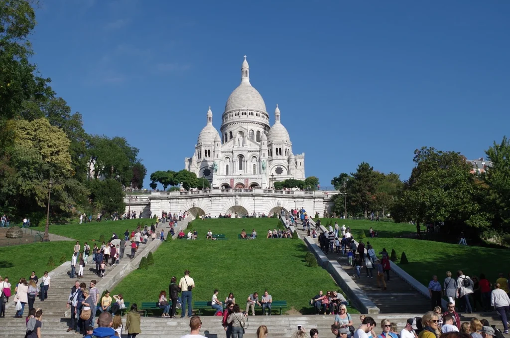 Paris Gezi Rehberi içeriğimizde öne çıkan Montmartre tepesinden görünen, bembeyaz kubbeli Sacré-Cœur Bazilikası’na doğru çıkan geniş basamaklarda ve yemyeşil çimenlik alanlarda güneşli bir günde keyifli vakit geçiren yoğun insan kalabalığı.