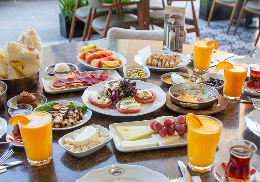 Geniş bir masaya özenle serilmiş; domatesli mozzarella, hellim ızgara, peynir çeşitleri, zeytinler, sucuklu yumurta, sıcacık börek, taze ekmekler, bol köpüklü çay ve portakal suyu gibi birçok enfes lezzetle dolu bu pazar kahvaltısı, şeflerin lezzet rotalarındaki unutulmaz duraklardan birini gözler önüne seriyor.