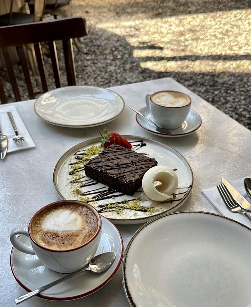 İstanbul'un en güzel bahçeli mekânlarından birinde, güneşin huzurlu ışıklarıyla aydınlanan bir masada, latte art desenli iki sıcak kahve ve çilek, fıstık kırıntılarıyla zenginleştirilmiş, soslu bir çikolatalı brownie tatlısının eşlik ettiği keyifli bir an.