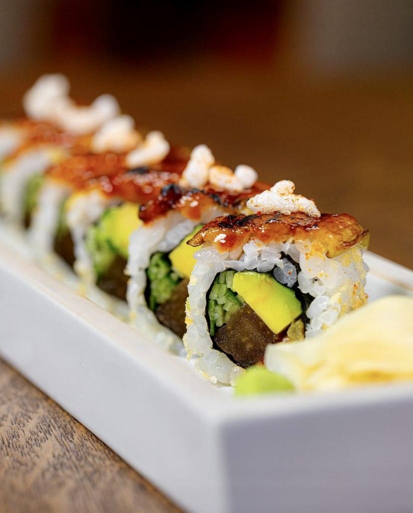 Görselde, beyaz bir servis tabağında, üstü ızgara yılan balığı sosu ve minik karideslerle zenginleştirilmiş, içinde taze avokado dilimleri bulunan iştah açıcı sushi ruloları, yanında wasabi ve zencefil turşusuyla sunuluyor; bu enfes sunum, İstanbul'un en iyi teraslı mekanlarında tadılabilecek çok çeşitli dünya lezzetlerinden sadece biri.