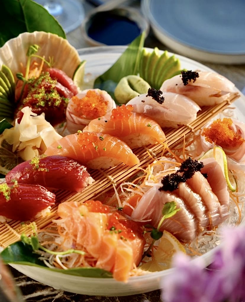 Büyük bir tabakta zarifçe sunulmuş, somon, ton balığı ve beyaz balık nigiri ile sashimi çeşitleri, üzerleri parlak havyar ve siyah havyarla süslenmiş, taze zencefil ve limon dilimleriyle bezenmiş bu görsel, İstanbul'un en popüler sushi restoranlarında sunulan kaliteli sushi lezzetlerini yansıtıyor.