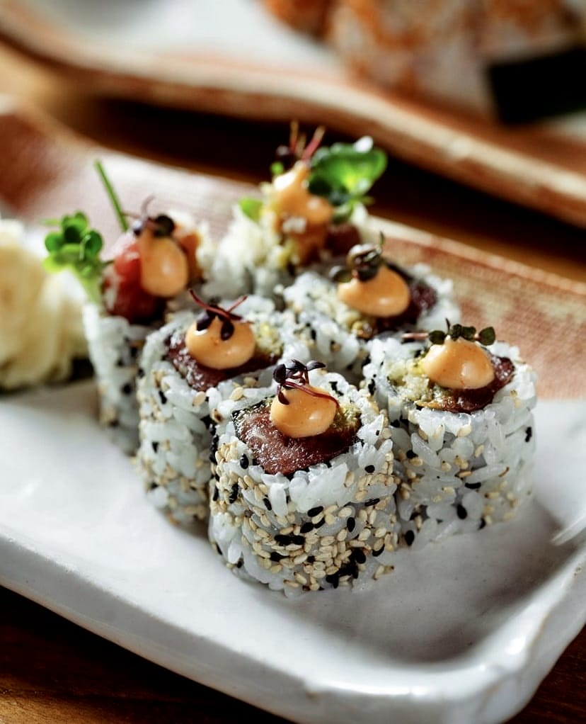 Beyaz bir tabakta, susam taneleriyle kaplı, taze ton balığı ve kremalı sos ile filizlerle özenle süslenmiş altı adet sushi rulosu, İstanbul'un en iyi sushi restoranlarının sunum kalitesini gözler önüne seriyor.