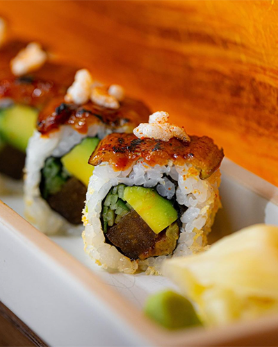 Beyaz bir tabakta özenle sunulan, parlak soslu ve çıtır dokunuşlarla zenginleştirilmiş unagi ve avokado dolgulu uramaki sushi ruloları, taze zencefil ve wasabi eşliğinde, İstanbul'un en popüler sushi restoranlarında sunulan rafine lezzetleri yansıtıyor.
