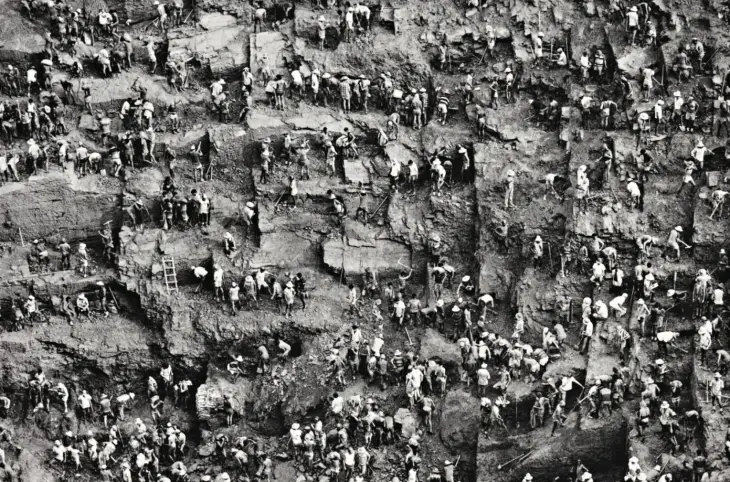 Büyük bir yamaçta, altın madeni içinde çalışan çok sayıda işçi; kazı yapan insanlar toplu halde görülüyor.