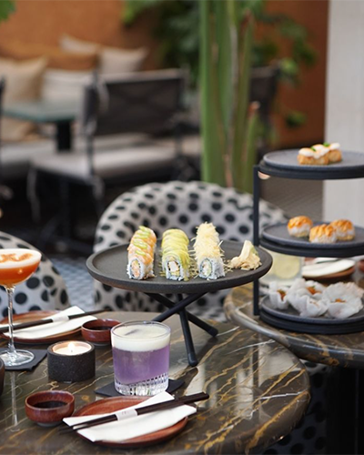 İstanbul’un en iyi sushi restoranlarından birinde, mermer bir masanın üzerinde özenle hazırlanmış yeşil avokadolu ve çıtır tempuralı roll çeşitleri, katlı serviste buharda pişmiş Uzak Doğu lezzetleri ve mor renkli kokteyllerle dolu şık bir sunum, modern bir ambiyansta keyifli bir sushi deneyimi vadediyor.
