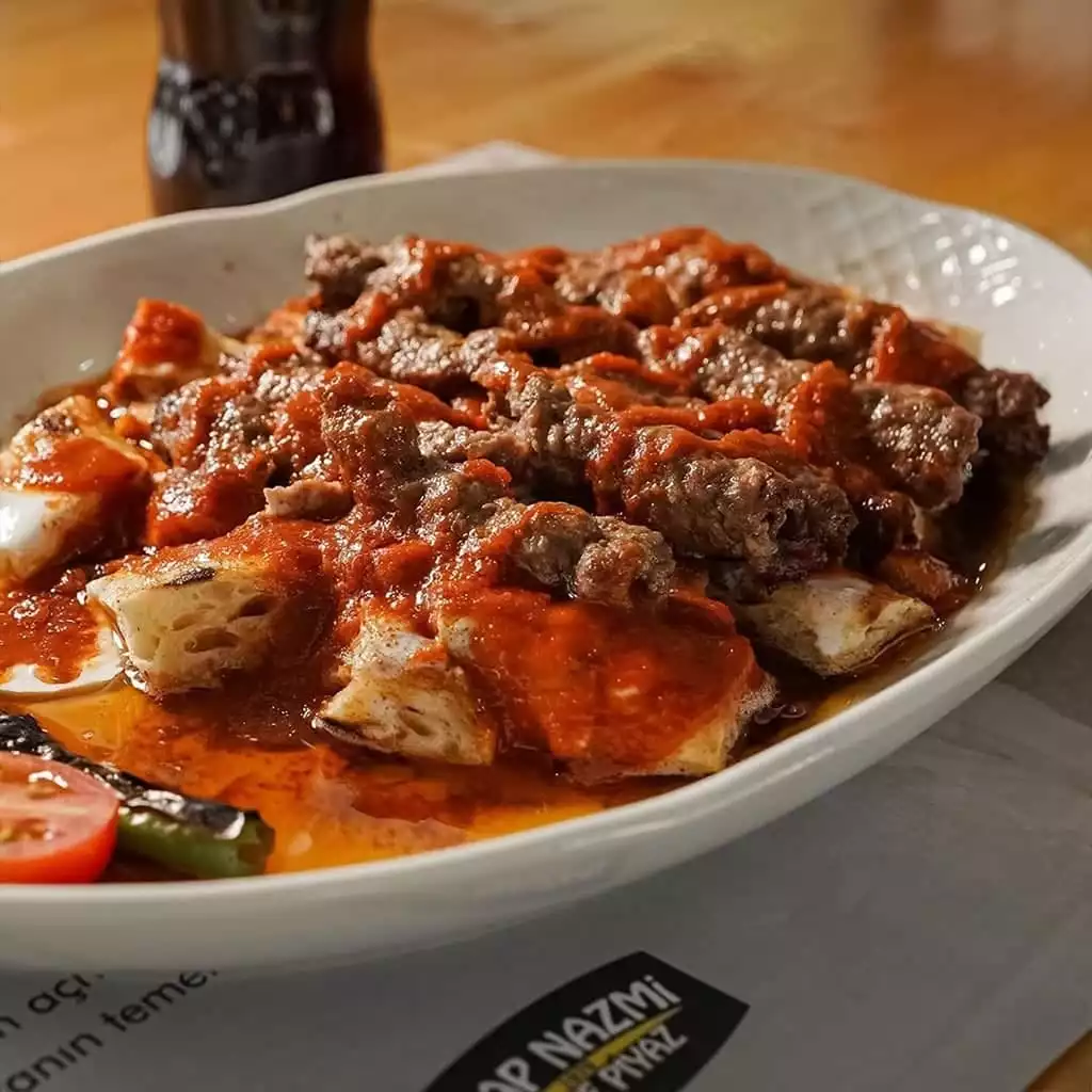 Antalya'nın köklü restoranlarından Arap Nazmi'de, kızarmış pide parçaları üzerinde bol domates sosuyla servis edilen iştah açıcı şiş köfteler, yanında ızgara biber, domates ve bir parça yoğurtla yöresel bir lezzet şöleni sunuyor.
