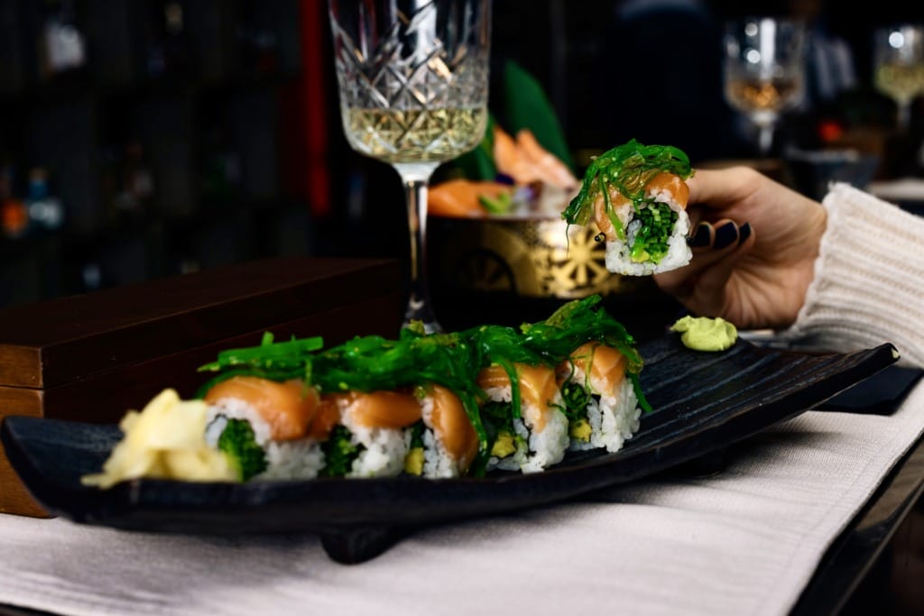 Bir elin zarifçe chopsticklerle kaldırdığı, üzerinde taze somon ve parlak yeşil wakame yosunu bulunan, şık siyah bir tabakta özenle dizilmiş maki sushi ruloları, İstanbul’un popüler sushi restoranlarından birindeki rafine Uzak Doğu lezzetlerini ve kaliteli sunumu vurguluyor.