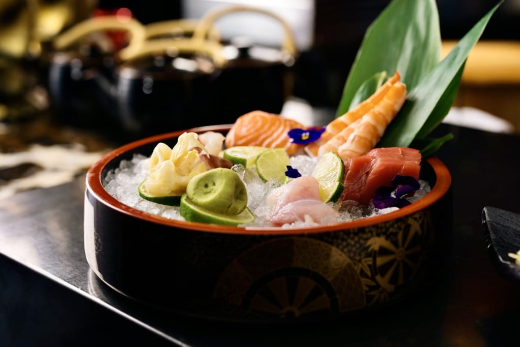 Buz üzerinde taze somon, orkinos, karides dilimleri, yanında misket limonu, wasabi ve zencefil turşusu ile sunulan bu göz alıcı sashimi tabağı, İstanbul'un en popüler sushi restoranlarında sunulan Uzak Doğu lezzetlerinin tazeliğini ve sunum kalitesini vurguluyor.