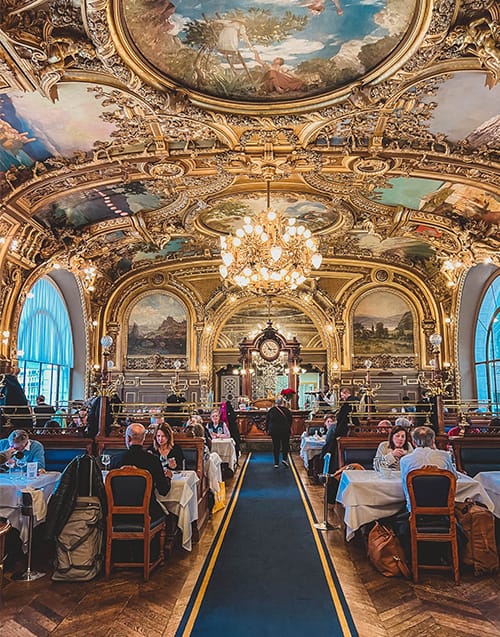 Gare de Lyon tren garında bulunan Le Train Bleu restoranının altın varaklı barok süslemeleri, fresklerle dolu tavanları ve görkemli avizelerle aydınlanan lüks iç mekanında, masa örtülü masalarda keyifle yemek yiyen misafirler Paris'in en iyi restoranları arasında unutulmaz bir deneyim yaşıyor.