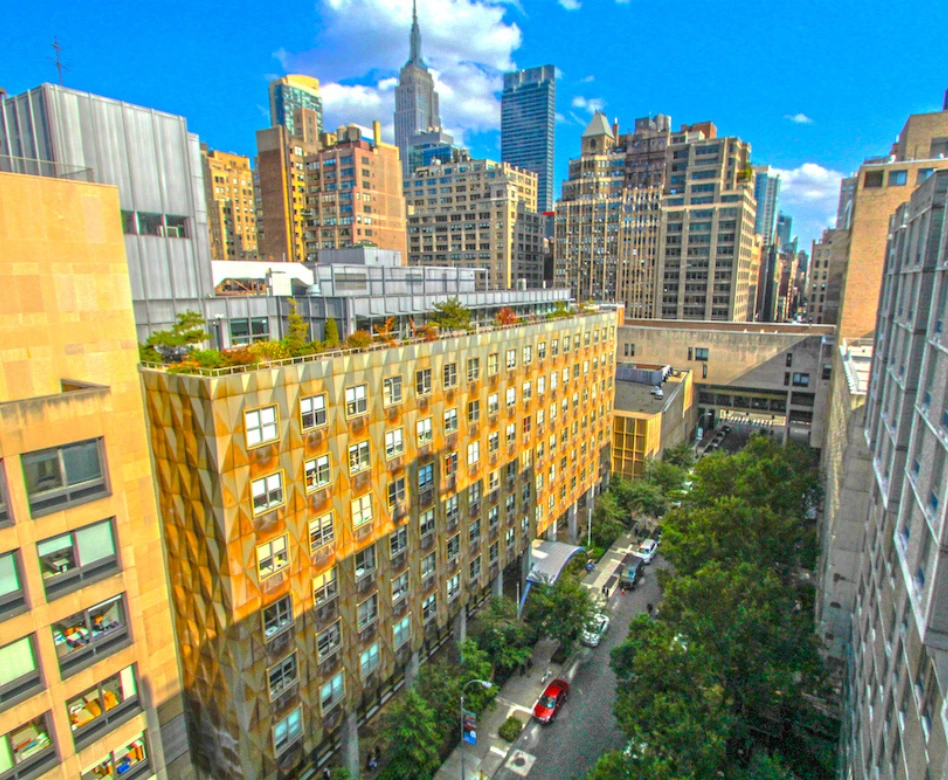 New York Şehri'ndeki Fashion Institute of Technology (FIT) kampüsünün yüksek açılı görüntüsü, geometrik tasarımlı cephesi ve yeşil çatılı bahçesiyle öne çıkan modern binasını, çevresindeki şehir manzarası ve gökdelenlerle birlikte gözler önüne sererek, dünyanın en iyi moda okulları arasında sayılan bu kurumun yenilikçi eğitim atmosferini vurguluyor.