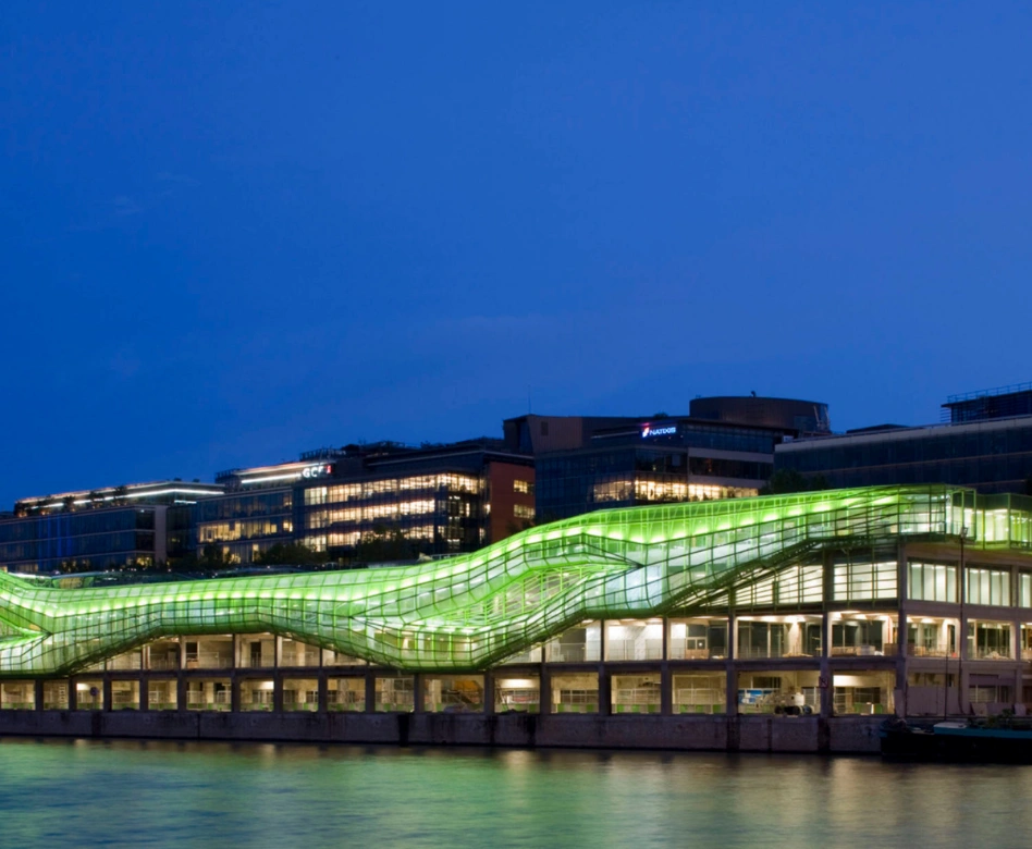 Gece karanlığında, Paris'teki bir moda okulunun yenilikçi mimarisini yansıtan, nehirden yansıyan parlak yeşil dalgalı cephesiyle modern bir bina, moda dünyasının geleceğine ışık tutuyor gibi duruyor.