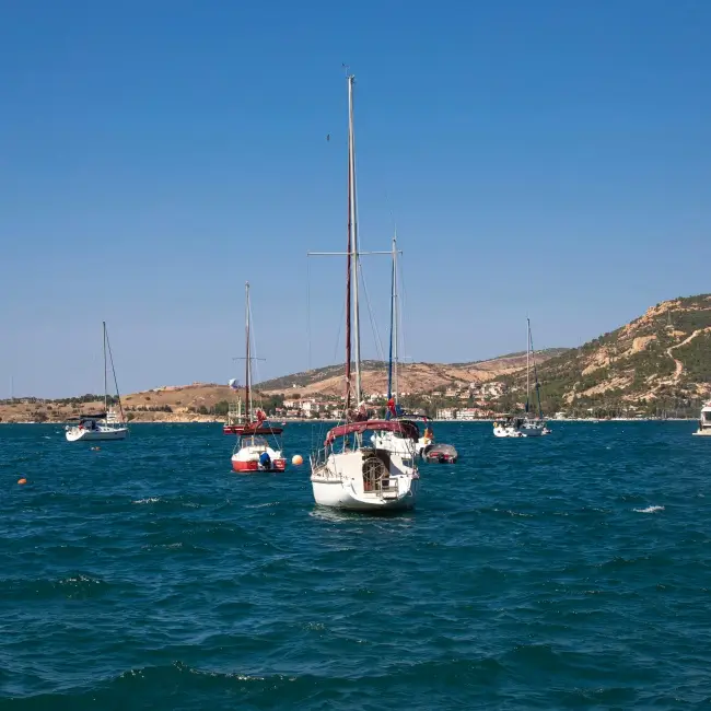 Masmavi Ege Denizi'nde demirlemiş yelkenli teknelerle dolu Foça koyu, arkasında yükselen yeşil tepelerle çevrili şirin sahil kasabası ve pırıl pırıl gökyüzüyle ziyaretçilerine huzurlu bir Ege tatili vaat ediyor.