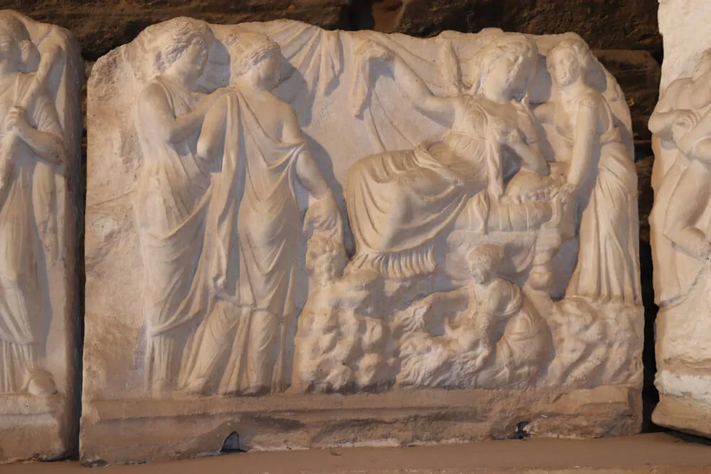 Hierapolis Antik Kenti'nden kalma, Pamukkale'nin zengin tarihi dokusunu yansıtan bu beyaz mermer kabartma, antik dönemdeki yaşamdan sahnelerle birlikte, oturan ve ayakta duran figürleri detaylı draperilerle zarifçe tasvir etmektedir.