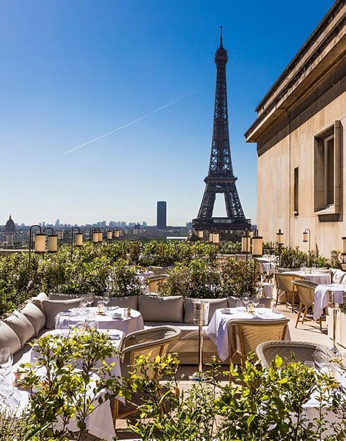 Eyfel Kulesi'nin tam karşısında yer alan yemyeşil bitkilerle çevrili lüks bir Paris restoranının terasında, beyaz örtülü masalar ve konforlu koltuklar misafirleri muhteşem şehir manzarası eşliğinde bekliyor.