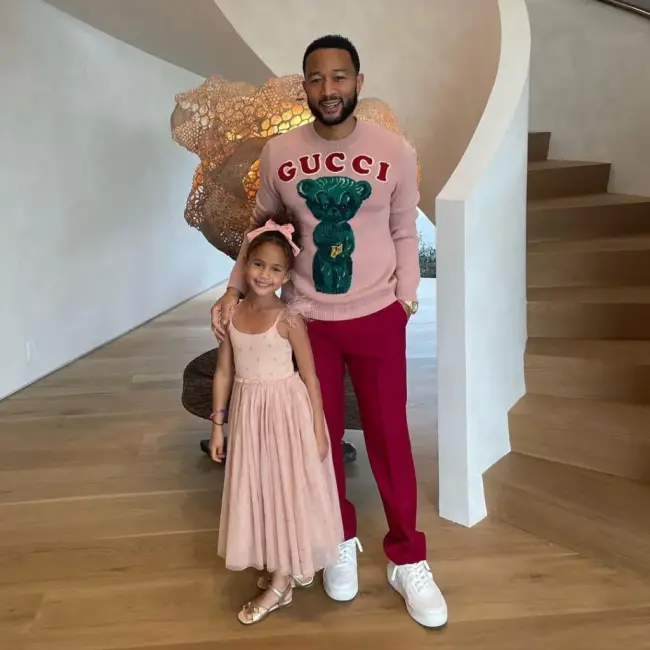 John Legend ve kızının, uyumlu pembe tonlarında kıyafetler giyerek merdiven boşluğunda şık bir şekilde poz verdikleri bir iç mekan çekimi.