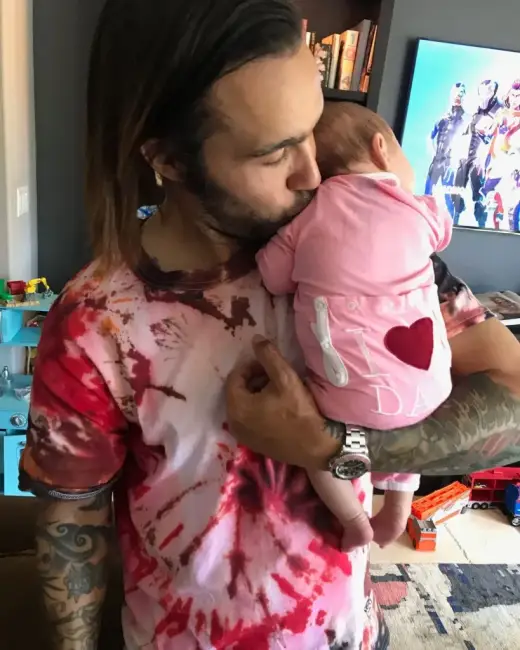 Pete Wentz olduğu anlaşılan bir baba, kollarında pembe tişört giyen bir bebeği tutarken onu öpüyor, her ikisi de renkli tişörtler giyiyor.